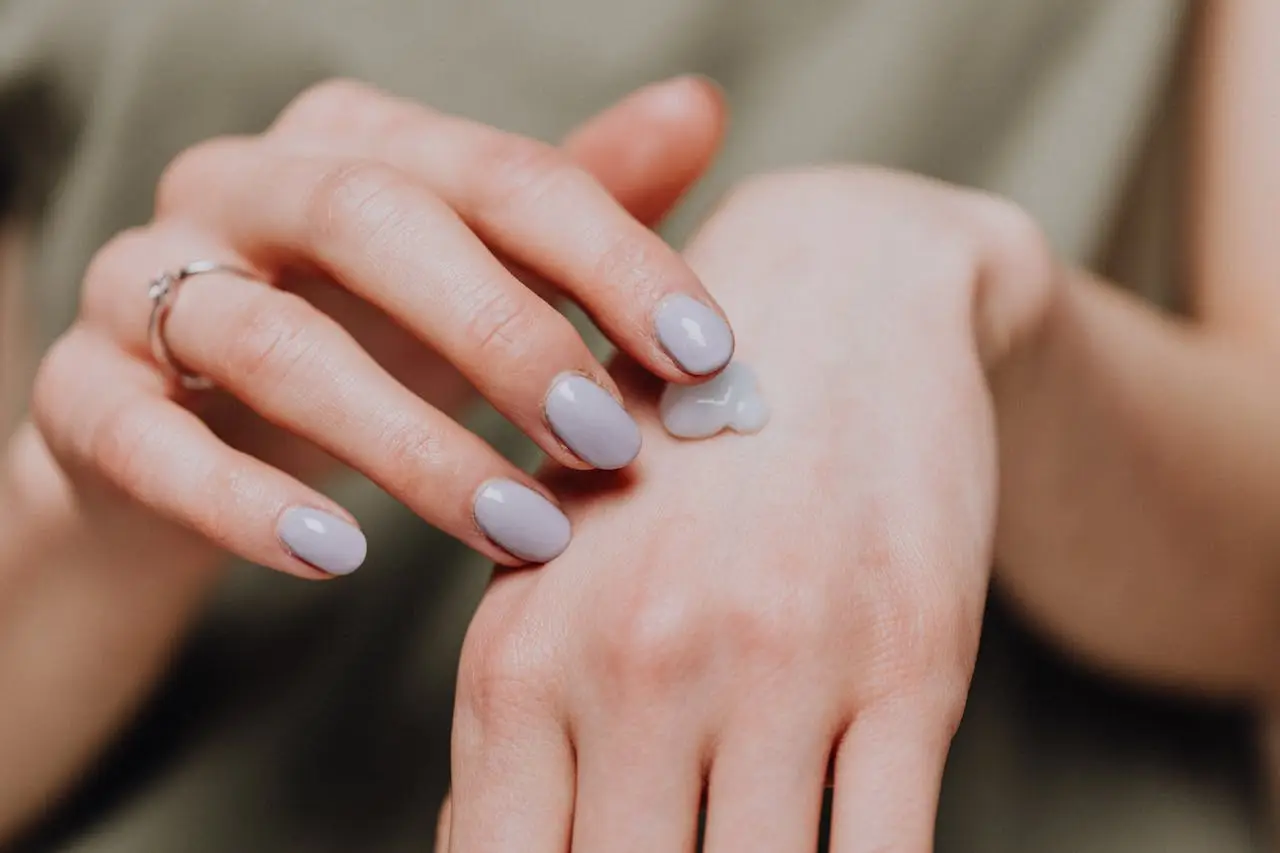 A woman's hand applying moisturizing cream, emphasizing skincare and nail beauty.
